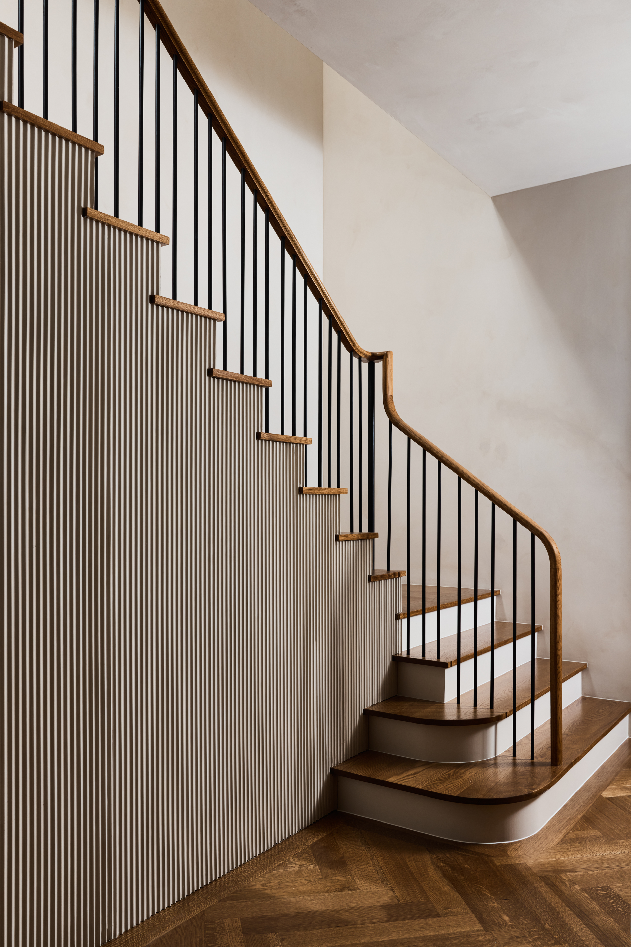 Curving oak stair rail with slender black balusters